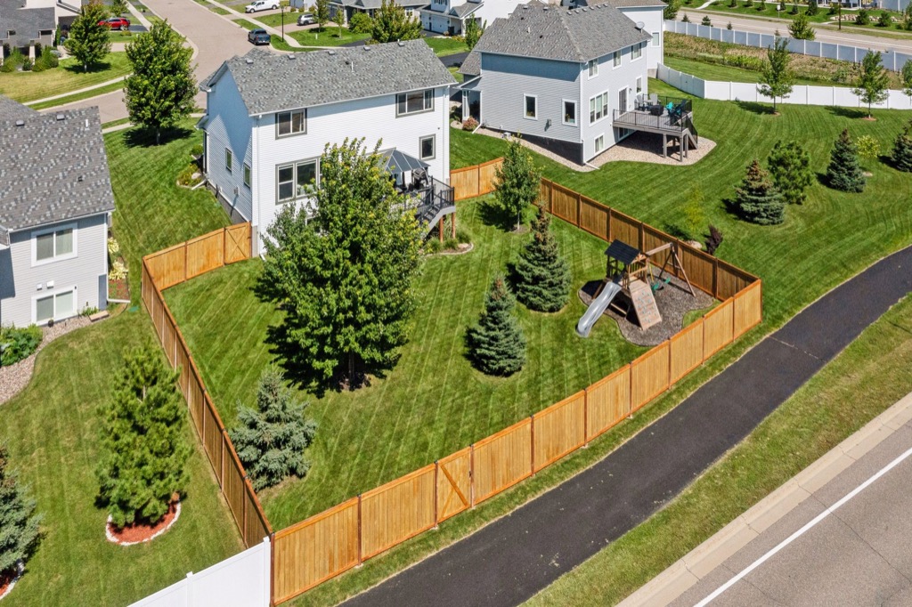 Aerial view of a suburban backyard on Fairchild Way with a wooden fence, green lawn, several trees, and a childrens playset with a slide, surrounded by neighboring houses and street—perfect for memorable photos. Ref 15668.