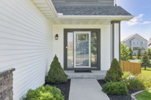A modern house entrance on Fairchild Way features white siding, a glass storm door, concrete steps, two green shrubs on each side, and a manicured lawn in the background. See PHOTOS for more details.