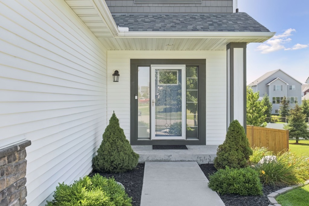 A modern house entrance on Fairchild Way features white siding, a glass storm door, concrete steps, two green shrubs on each side, and a manicured lawn in the background. See PHOTOS for more details.