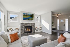 Bright living room on Fairchild Way with a stone fireplace, wall-mounted TV, light gray sectional and orange pillows. White built-ins flank the fireplace. Sunlight streams in near the double-door entryway—see PHOTOS for details.