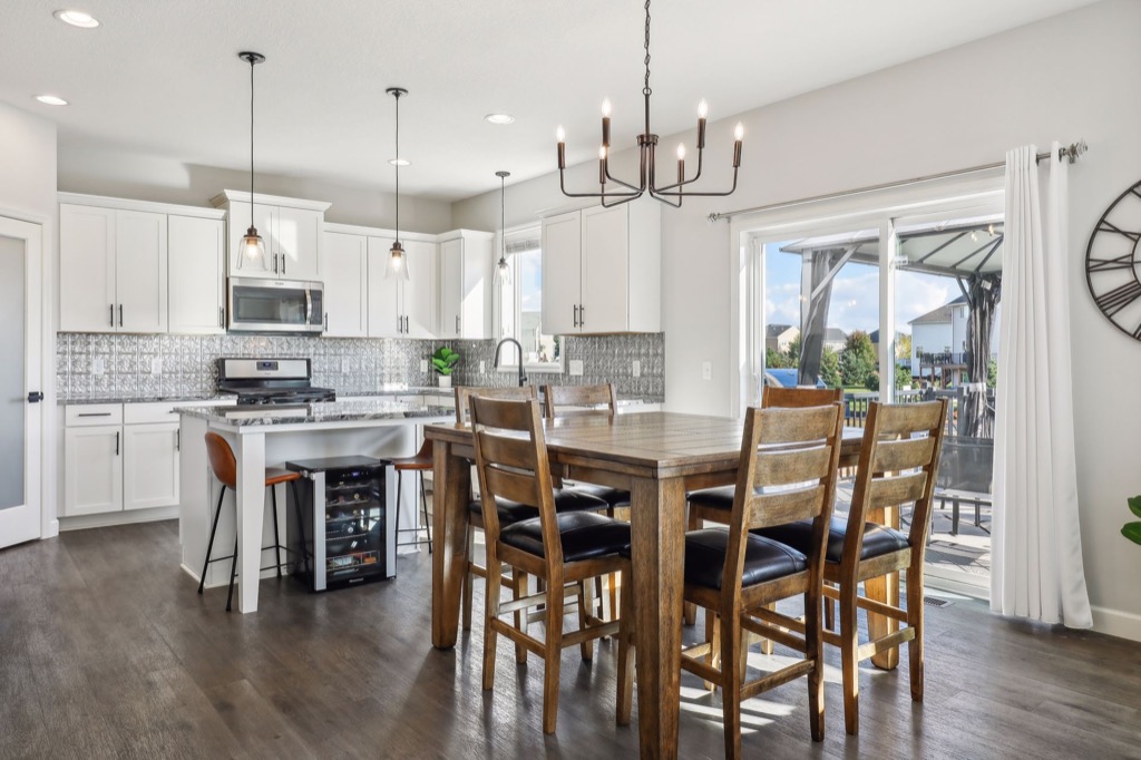 Bright, modern kitchen and dining area at 15668 Fairchild Way, with white cabinets, stainless steel appliances, a wooden dining table for six, pendant lights, and sliding glass doors to a sunny patio. See PHOTOS for details.