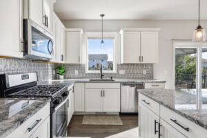 Modern kitchen with white cabinets, stainless steel appliances, marble countertops, and an island. A window above the sink fills the space with light. Silver backsplash and pendant lights add style. See more PHOTOS of 15668 Fairchild Way.