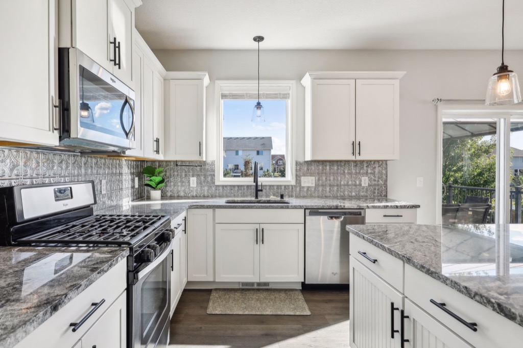 Modern kitchen with white cabinets, stainless steel appliances, marble countertops, and an island. A window above the sink fills the space with light. Silver backsplash and pendant lights add style. See more PHOTOS of 15668 Fairchild Way.