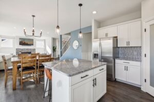 Bright modern kitchen and dining area on Fairchild Way with white cabinets, stainless steel appliances, granite island, pendant lights, wooden dining table, and blue accent wall near a staircase. See PHOTOS for more details.