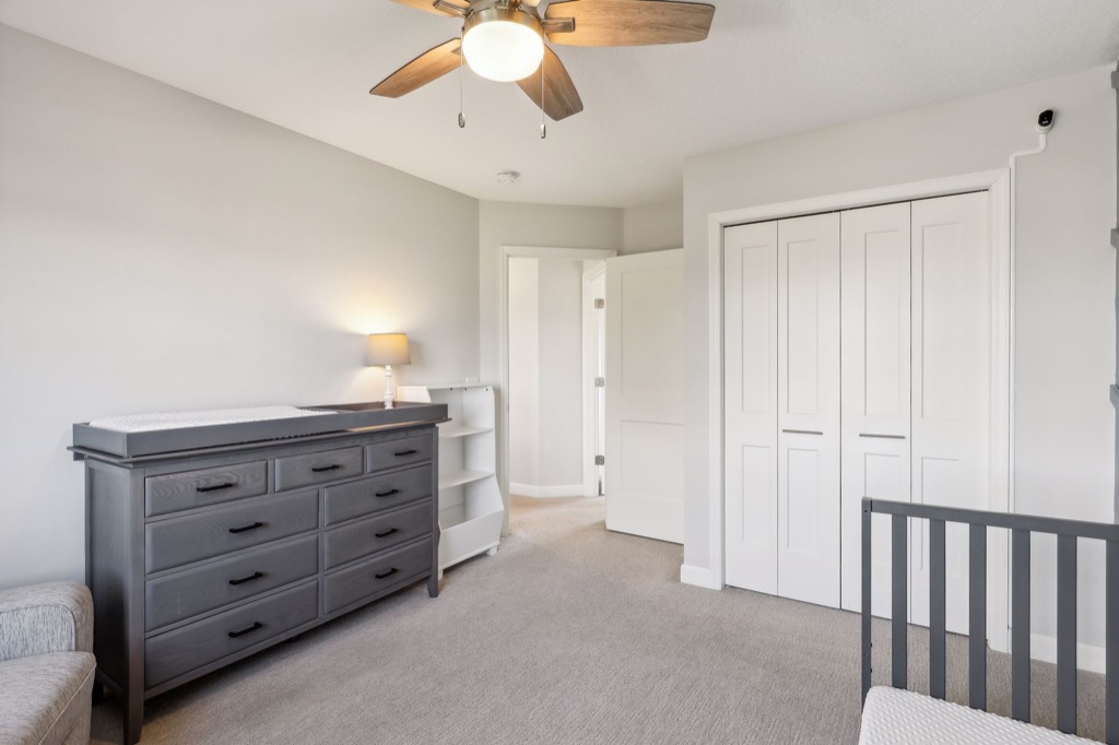 A bright, neutral-colored nursery at 15668 Fairchild Way features a ceiling fan, gray dresser with changing pad, small white bookshelf, closed closet doors, part of a crib in the foreground—see PHOTOS for more detail.