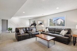 A modern, spacious living room on Fairchild Way, 15668, with two black leather sofas, a wooden coffee table, neutral carpet, and large windows letting in natural light. PHOTOS show a treadmill positioned by the window in the background.