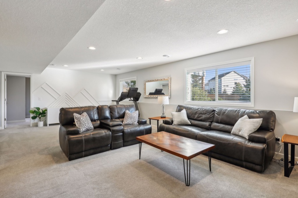 A modern, spacious living room on Fairchild Way, 15668, with two black leather sofas, a wooden coffee table, neutral carpet, and large windows letting in natural light. PHOTOS show a treadmill positioned by the window in the background.