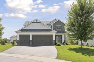A modern two-story suburban house on Fairchild Way with a three-car garage, gray siding, white trim, and a large driveway, surrounded by a well-kept green lawn and trees under a partly cloudy sky. PHOTOS available upon request.