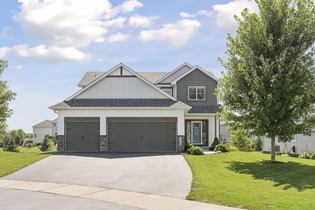 A modern two-story suburban house on Fairchild Way with a three-car garage, gray siding, white trim, and a large driveway, surrounded by a well-kept green lawn and trees under a partly cloudy sky. PHOTOS available upon request.