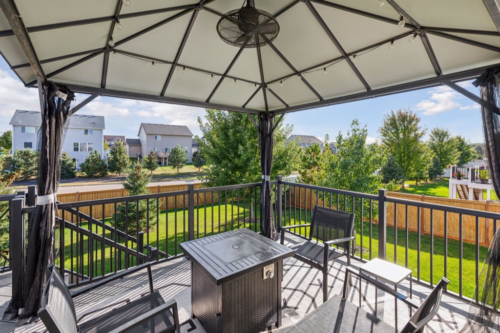A covered patio with a metal gazebo, table with fire pit, and several chairs overlooks the fenced backyard at 15668 Fairchild Way—lush grass, trees, and neighboring houses create a perfect scene for PHOTOS on a sunny day.