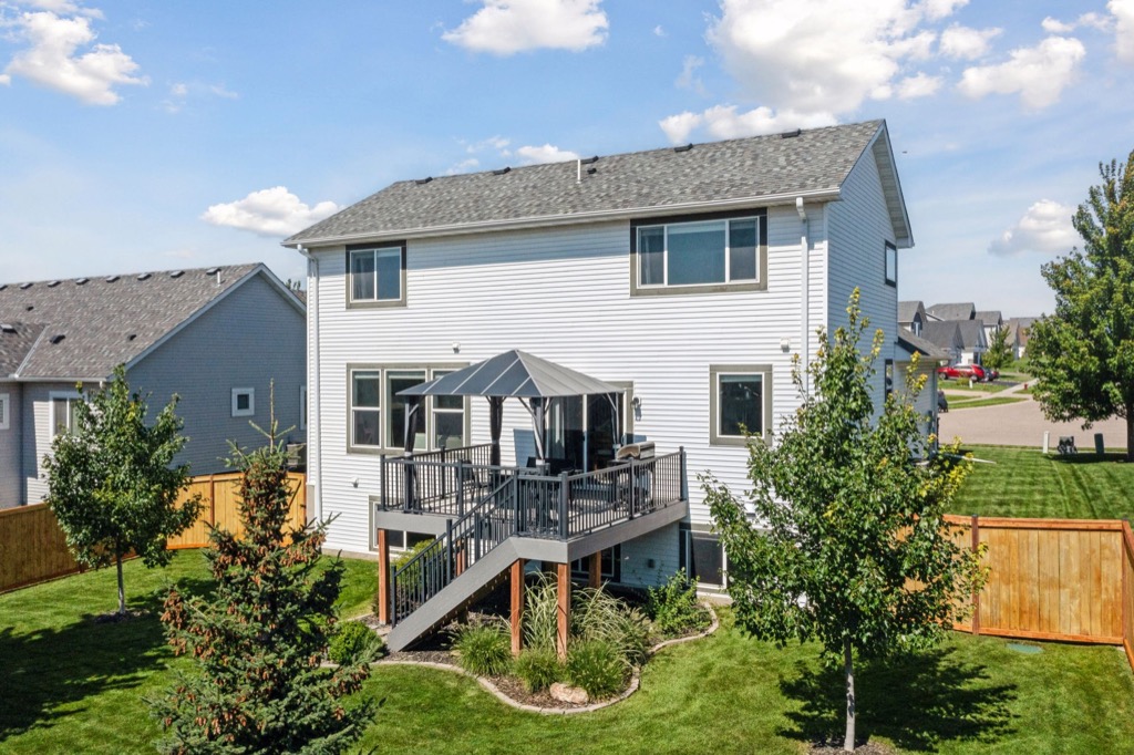 Two-story white house with a gray roof at 15668 Fairchild Way. Enjoy the fenced backyard with an elevated deck, patio furniture, and umbrella. Stairs lead to the green lawn and trees, all under a blue sky. See PHOTOS for more details!.