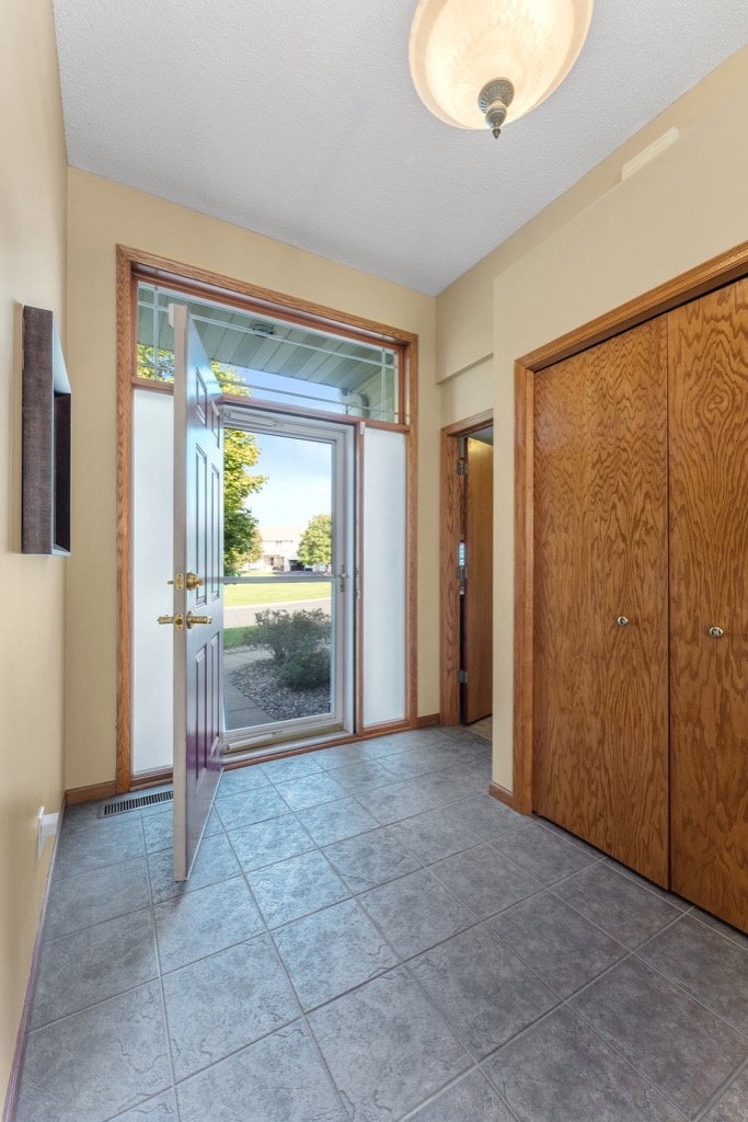 A bright entryway at Whitehall Place features light yellow walls, a tiled floor, wooden closet doors on the right, and a glass-paneled front door open to a sunny view—captured in stunning Whitehall Place photos.