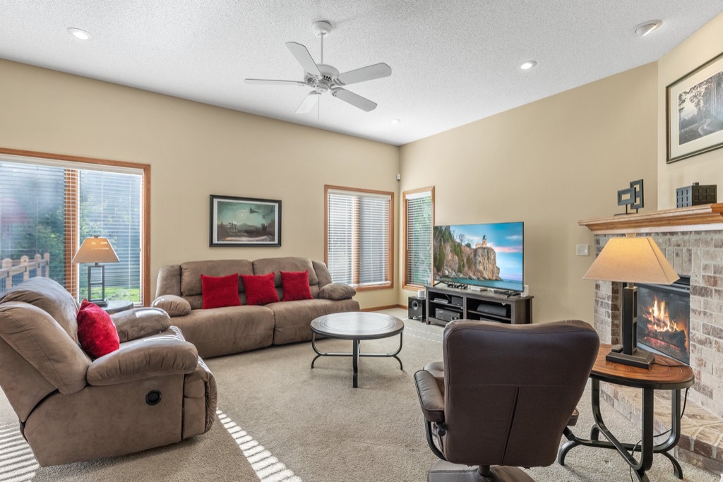 A cozy living room at Whitehall Place features beige walls, two brown sofas with red cushions, a round coffee table, a TV on a stand, a brick fireplace, and large windows brightening the space—perfect for real estate PHOTOS 1648.