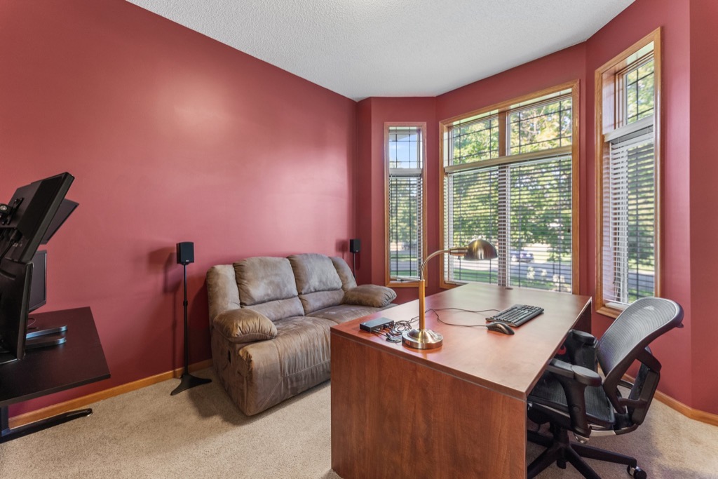 A home office at 1648 Whitehall Place features red walls, a brown desk with a lamp and computer, an office chair, a brown reclining loveseat, and large windows with blinds letting in natural light. See PHOTOS for more details.