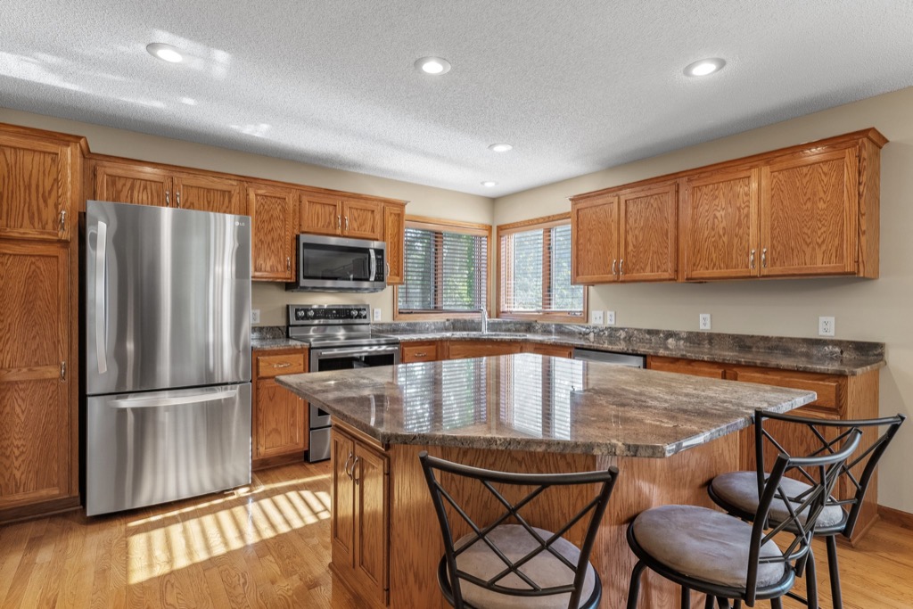 Spacious kitchen at 1648 Whitehall Place with wooden cabinets, stainless steel appliances, large marble island with two chairs, and windows letting in natural light. See PHOTOS for more details.