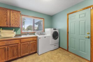 A laundry room at 1648 Whitehall Place features wood cabinets, a countertop with a basket, a sink, a top-load washer, and a front-load dryer beside a green door and window with blinds. See PHOTOS for more details.