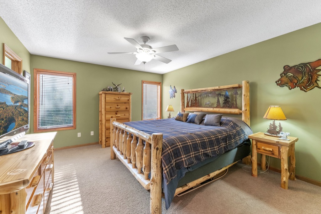 Rustic bedroom at 1648 Whitehall Place with log furniture, plaid bedding, green walls, bear and nature-themed decor. Two windows with white blinds, ceiling fan with light, carpeted floor, natural wood accents—see PHOTOS for details.