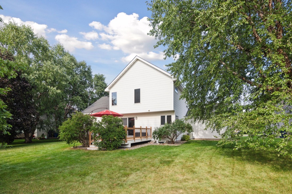PHOTOS of 1648 Whitehall Place: A white two-story house with a wooden deck and red patio umbrella, surrounded by green grass, trees, and shrubs under a partly cloudy sky.