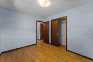 Empty room with light blue walls, wooden floor, two wooden doors (one open to a closet), and a ceiling light; baseboard and door trim are dark wood.