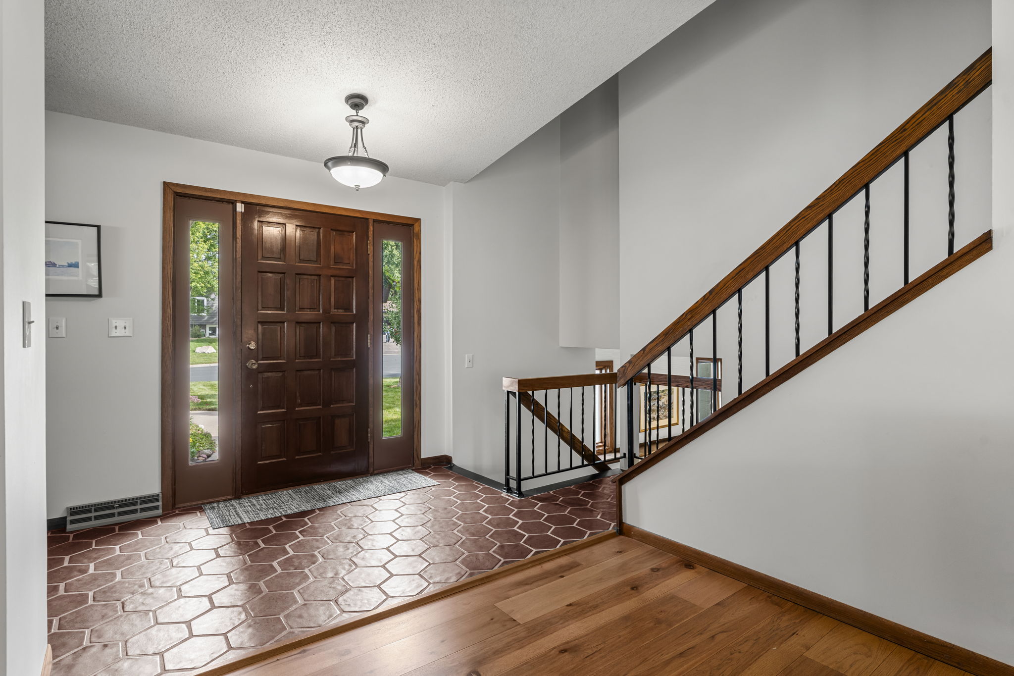 A spacious entryway at 9333 Colorado Circle features a wooden front door, hexagonal tile flooring, and a staircase with black balusters. Light gray walls and abundant natural light welcome you to this Minnesota home by Beekeeper Realty.