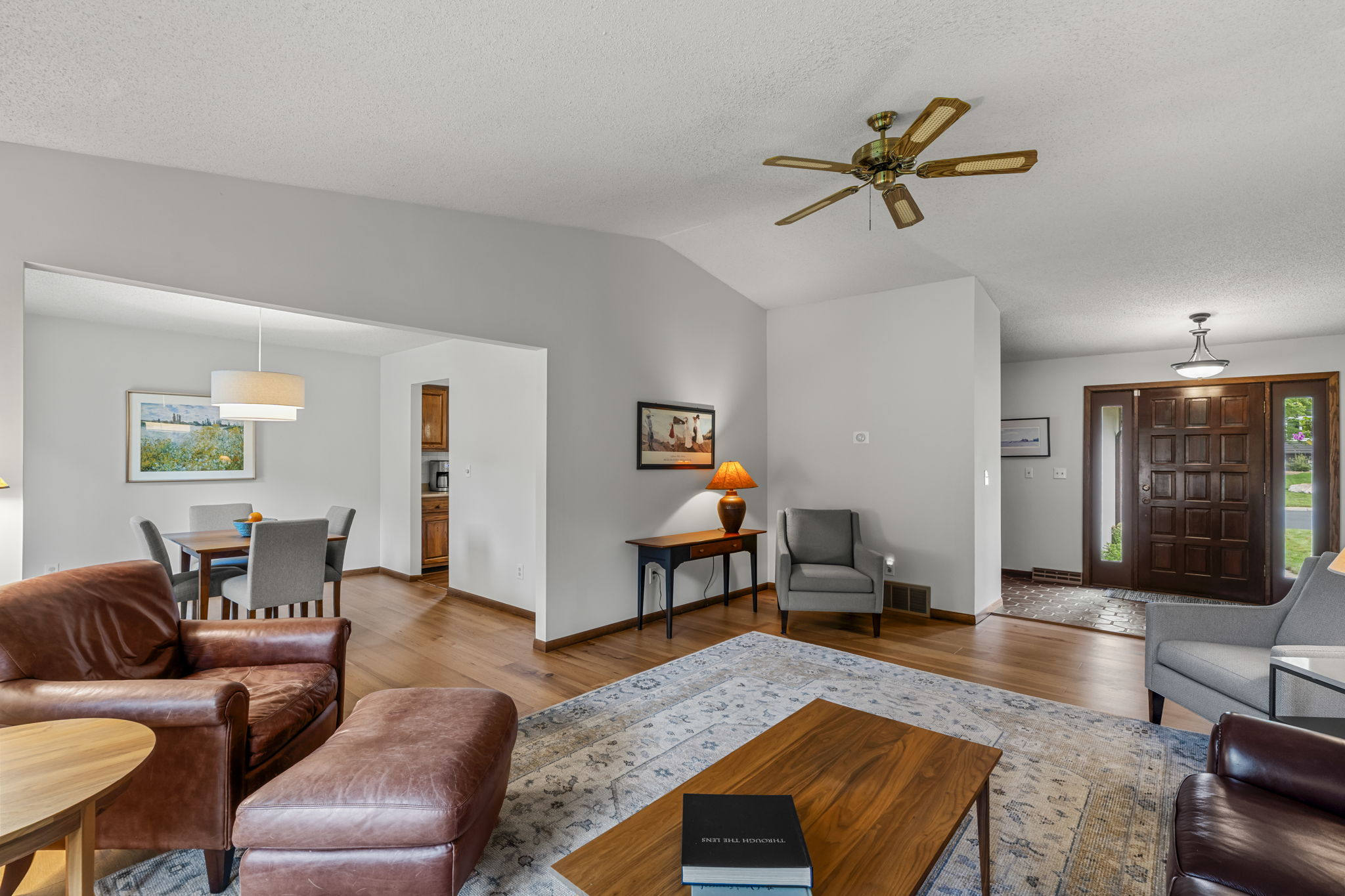 A bright living room with wood floors, leather and fabric seating, a wooden coffee table, and ceiling fan. Enjoy views into the dining area and front door with sidelights in this beautiful home for sale by Beekeeper Realty at 9333 Colorado Circle.