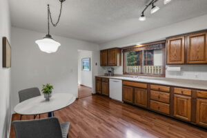 A kitchen in Bloomington with wooden cabinets, white countertops, and hardwood floors. A small round dining table with two gray chairs and a potted plant sits to the left. Large windows overlook the patio at 9333 Colorado Circle, Minnesota.