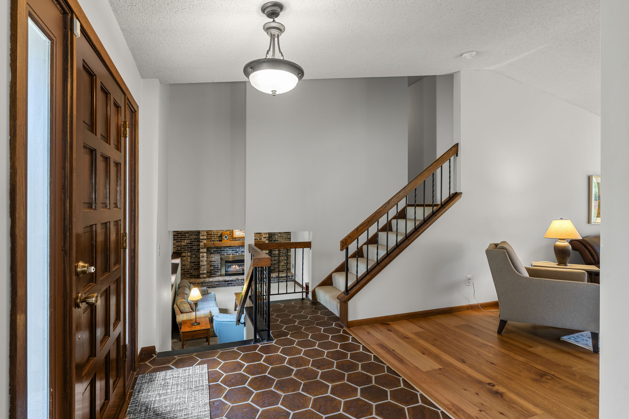 This Minnesota home entryway at 9333 Colorado Circle showcases a wooden front door, hexagonal tile flooring, stairs with a wooden banister, and views into the living room and lower level. Listed by Beekeeper Realty.
