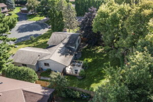 Aerial view of a suburban house with a fenced backyard, wooden deck, shaded lawn, and large trees at 9333 Colorado Circle—this quiet neighborhood gem is a home for sale by Beekeeper Realty.