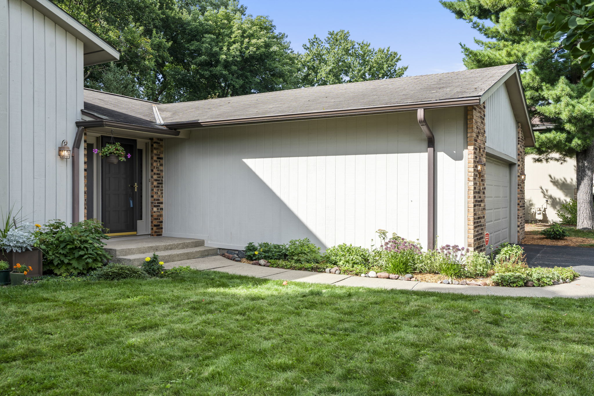 Charming single-story house in Bloomington, Minnesota, featuring light-colored siding, brick accents, a two-car garage, and a dark front door with a flower wreath. Enjoy a small garden bed, green lawn, and trees at 9333 Colorado Circle.