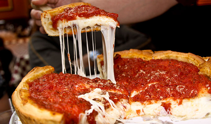 A deep-dish pizza with a thick crust and chunky tomato sauce is sliced open at 4424 Louisiana Ave N Crystal, revealing gooey, stretchy melted cheese inside.